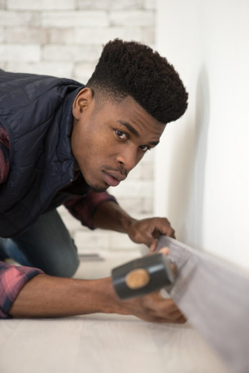 A young man installing a skirting board against the wall above a carpet floor